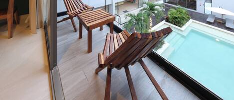 A balcony with wooden chairs and a pool.