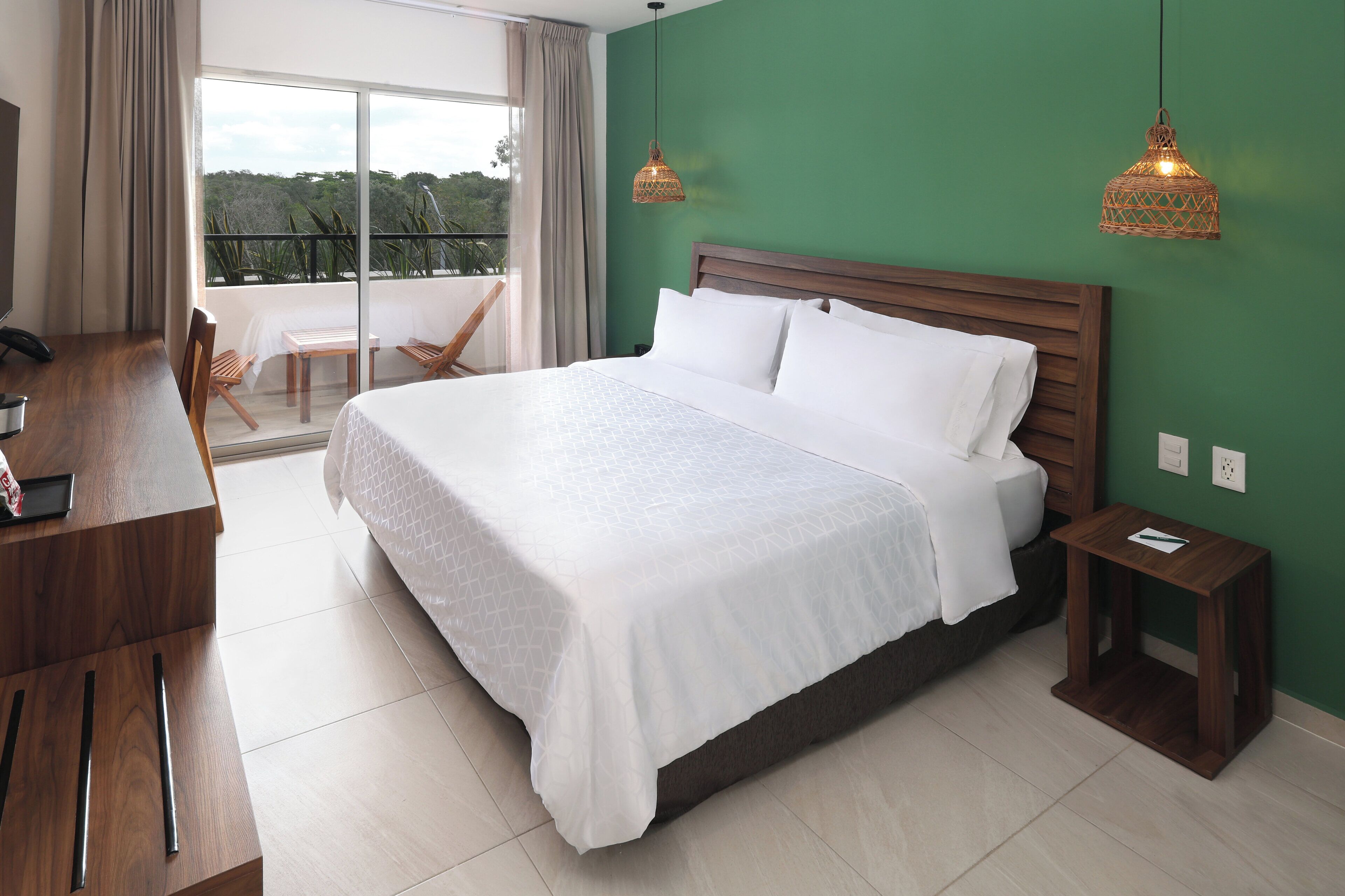 A hotel room with a large bed, a desk, a chair, and a view of the outdoors.