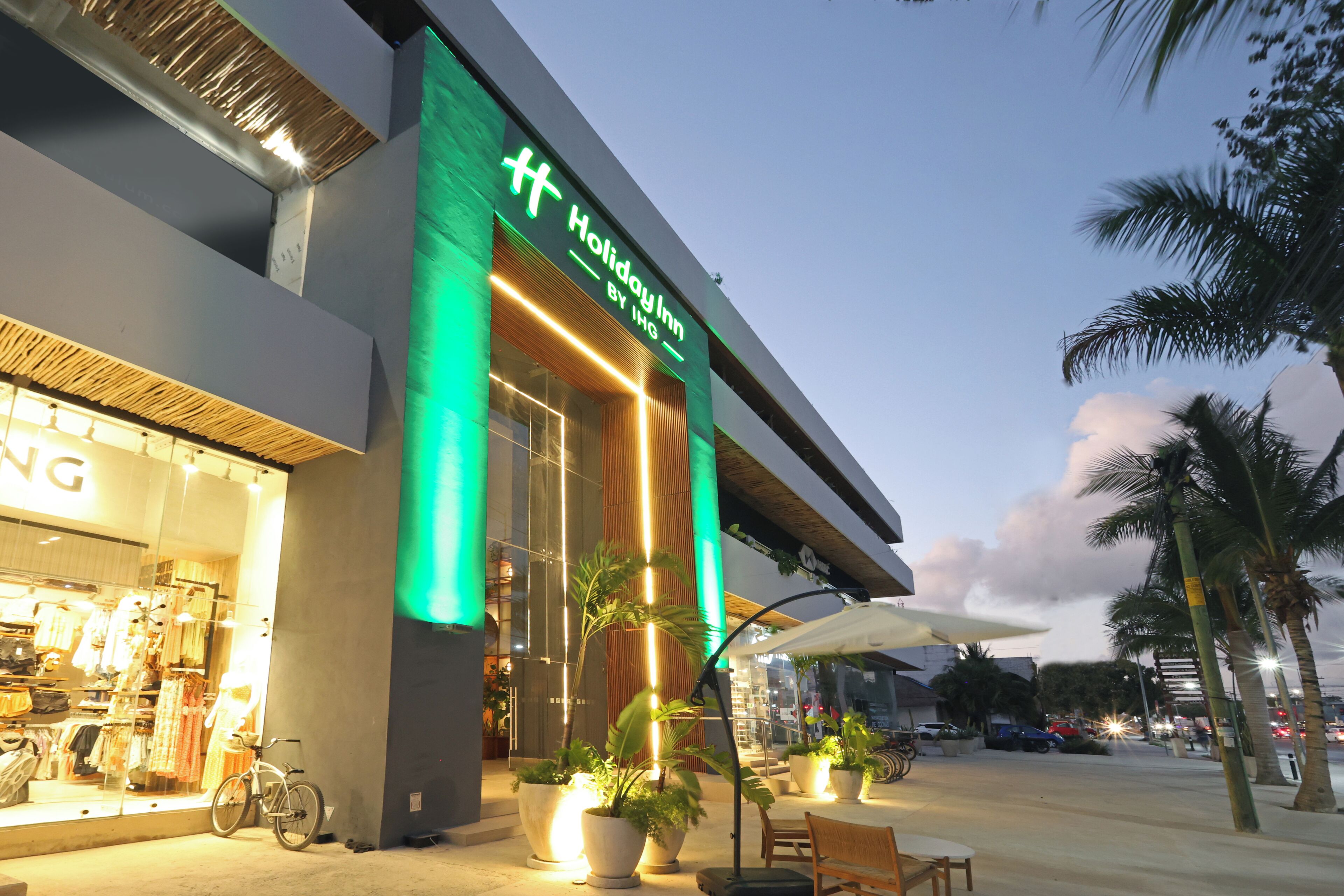 A Holiday Inn by IHG with a modern facade, outdoor seating, and palm trees.