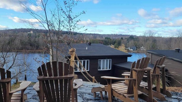 A lakeside cabin with wooden chairs and a deck overlooking the water.