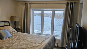 A bedroom with a bed, a lamp, a TV, and a window with a view of a lake.