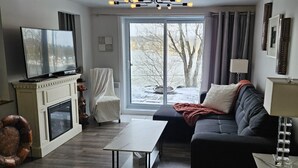 A living room with a fireplace, a sofa, a coffee table, a TV, and a view of a snowy landscape through a large window.