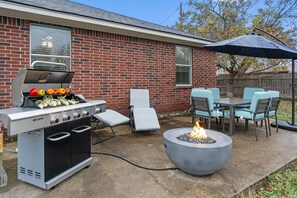 An outdoor patio with a gas grill, a fire pit, and outdoor seating.
