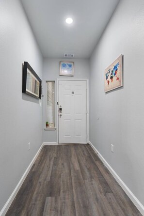 A hallway with a white door, a framed picture on the left, and a colorful abstract painting on the right.