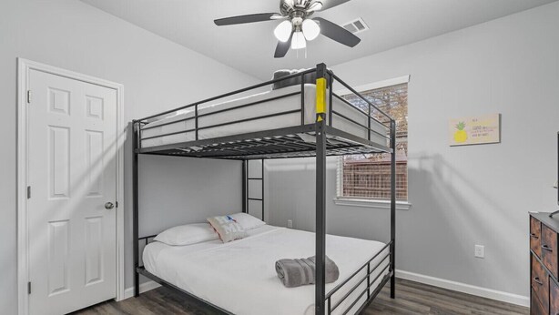 A bunk bed room with a ceiling fan, a window with blinds, and a wooden floor.