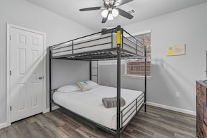 A bunk bed room with a ceiling fan, a window with blinds, and a wooden floor.