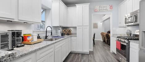 A modern kitchen with white cabinets, granite countertops, a built-in oven, and a microwave.