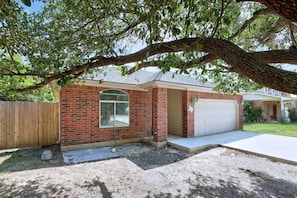 A single-story brick house with a garage, a large window, and a tree providing shade.