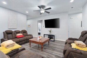 A modern living room with a ceiling fan, a flat-screen TV, and a coffee table.