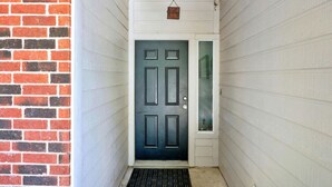 A narrow hallway with a dark door, white siding, and a brick wall on one side.
