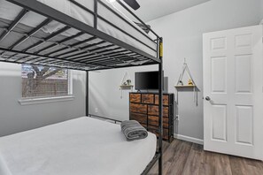 A bunk bed room with a TV on a wooden dresser, a white door, and a window with blinds.