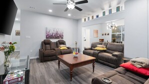 A modern living room with a sofa, two recliner chairs, a coffee table, and a ceiling fan.