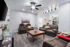 Ein modernes Wohnzimmer mit einer Couch, zwei Relaxsesseln, einem Couchtisch und einem Deckenventilator.