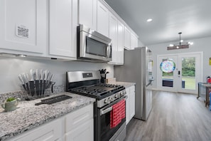 A modern kitchen with white cabinets, stainless steel appliances, granite countertops, and a red towel hanging on the oven.