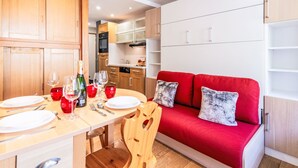Una cocina moderna con armarios de madera, una mesa de comedor con platos, vasos y cubiertos, y un sofá rojo con cojines estampados.
