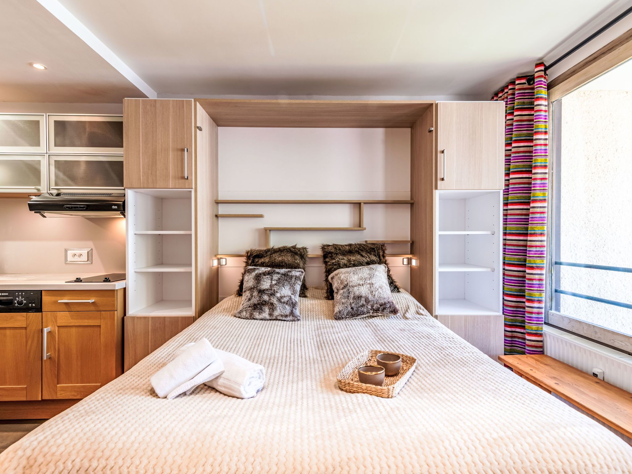 A modern bedroom with a built-in wardrobe, a bed with fluffy pillows, and a bedside table with a tray of items.