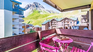 Un balcón con sillas rosas y una mesa, con vistas a un paisaje montañoso y edificios al fondo.