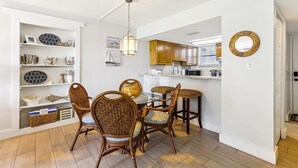 A dining area with wicker chairs and a glass table, a kitchen with wooden cabinets and a microwave, and a white wall with a round mirror. - Coquina A101 (St. Augustine)