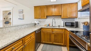 A kitchen with wooden cabinets, a stainless steel sink, a microwave, and a dishwasher. - Coquina A101 (St. Augustine)