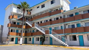 Egy többemeletes motel, központi lépcsőházzal, erkélyekkel és egy pálmafával az előtte lévő területen.