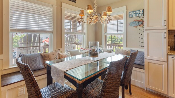 A dining area with a glass-top table, wicker chairs, and a chandelier. - 5178 Sea-Cryst * 3 Min Walk to Beach (Kill Devil Hills)