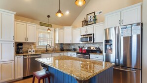 A kitchen with white cabinets, stainless steel appliances, granite countertops, and a central island with stools. - 5178 Sea-Cryst * 3 Min Walk to Beach (Kill Devil Hills)