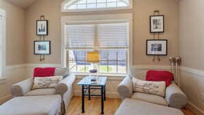 A cozy living room with two armchairs, a small table, and a window with blinds. - 5178 Sea-Cryst * 3 Min Walk to Beach (Kill Devil Hills)