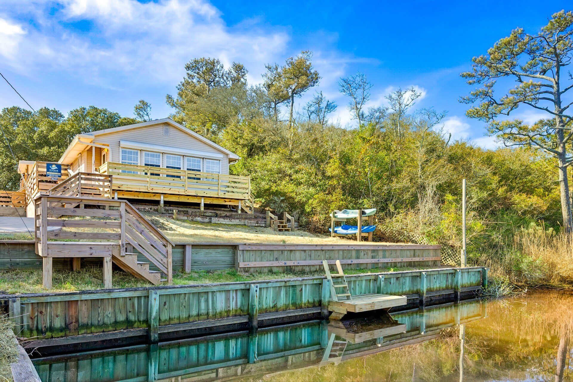 A wooden house with a deck and a dock extending into a calm body of water, surrounded by trees.