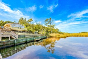 Une maison en bois dotée d’une terrasse et d’un petit quai pour bateaux, entourée d’arbres et bordée par une étendue d’eau calme.