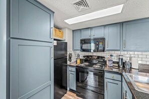 Une cuisine avec des meubles de couleur bleu clair, un réfrigérateur noir, un four à micro-ondes, une cuisinière et un évier.