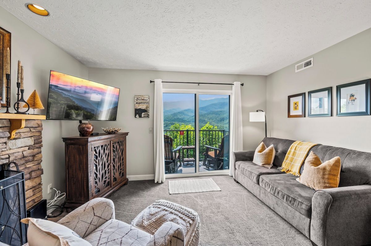 Een woonkamer met een bank, een televisie, een open haard en een balkon met uitzicht.