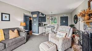 Een moderne woonkamer met een grijze bank, een fauteuil met een patroon, en een eethoek met een witte tafel en stoelen.
