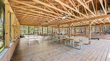An open pavilion with wooden beams, picnic tables, and benches.