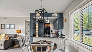 Un salon moderne comprenant un coin repas, une cuisine et de grandes fenêtres équipées de stores.