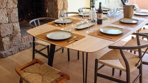 Un comedor con chimenea de piedra, mesa de madera y sillas de mimbre.
