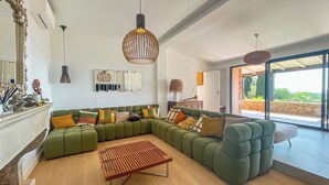 Una sala de estar moderna con un sofá seccional verde, una mesa de centro de madera y un ventanal con vistas a la vegetación.