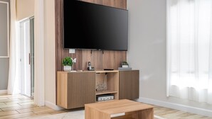 A modern living room with a flat-screen TV mounted on a wooden wall, a wooden coffee table, and a sliding door leading to a balcony.