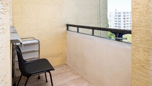 A small balcony with a black chair, a small table, and a view of a building.
