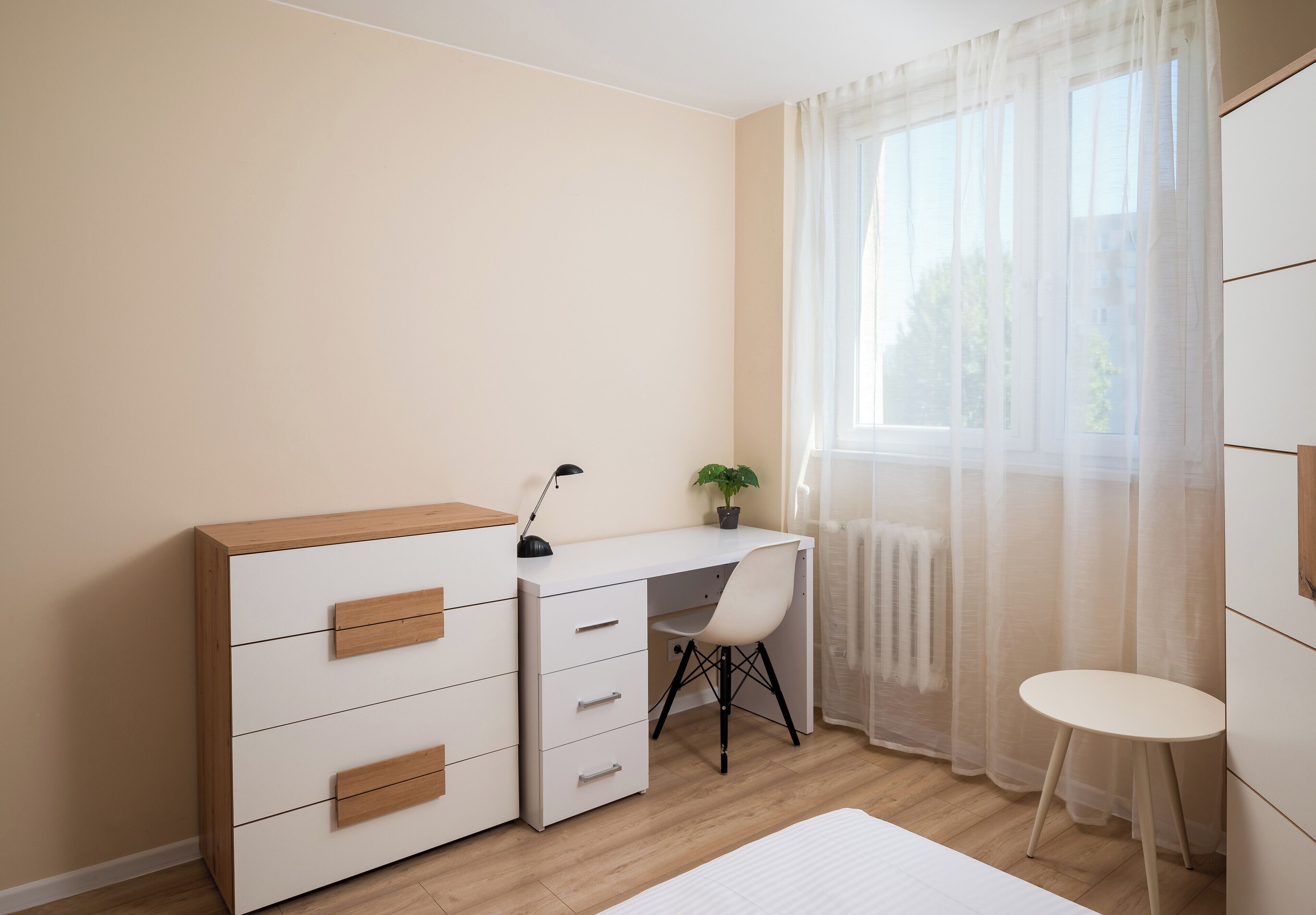 Une chambre à coucher comprenant un lit, un bureau avec des tiroirs, une chaise et une petite table.