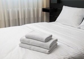 Ein ordentlich gemachtes Bett mit weißen Leinen und einem gefalteten Handtuch darauf, ein weißes Kopfkissen und ein schwarzer Nachttisch.