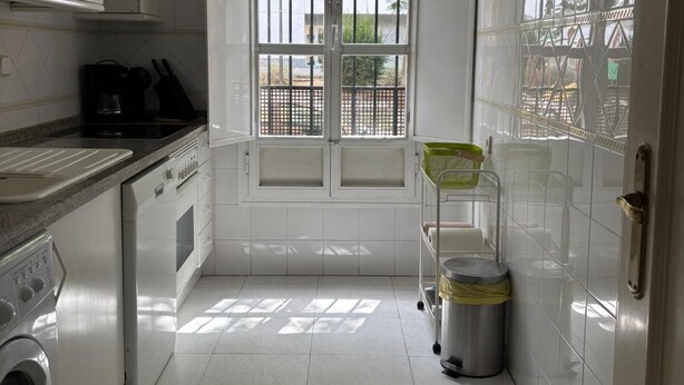A compact kitchen with white cabinets, a built-in oven, a washing machine, and a window with a view of the outside.