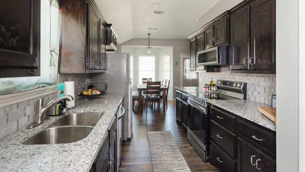 A kitchen with dark wooden cabinets, granite countertops, stainless steel appliances, and a dining area with a table and chairs.