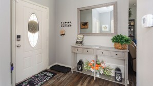 A hallway with a white door, a console table with a mirror, a small plant, and a welcome mat.