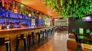 A bar area with wooden bar counter, black stools, hanging plants, and a television screen on the wall. - Garden views, island vibes near Napili Bay Beach (Lahaina)