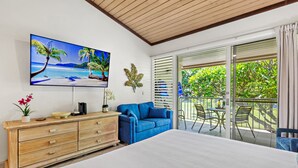 A bedroom with a large bed, a blue sofa, a wooden dresser, a TV on the wall, and a balcony with a view of greenery. - Garden views, island vibes near Napili Bay Beach (Lahaina)