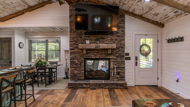 A rustic interior with a stone fireplace, wooden ceiling beams, and a dining area with a wooden table and chairs.