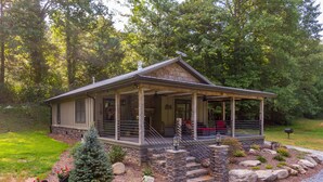 A rustic cabin with a covered porch, stone foundation, and a small front yard with a Christmas tree and potted plants.