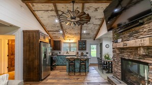 A rustic kitchen with a stone fireplace, wooden beams, and a large island with bar stools.