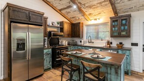 A kitchen with a stainless steel refrigerator, wooden cabinets, a central island with bar stools, and a rustic ceiling.