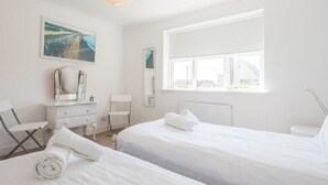 Ein helles, weißes Schlafzimmer mit zwei Betten, einem Schminktisch, einem Sessel und einem großen Fenster.